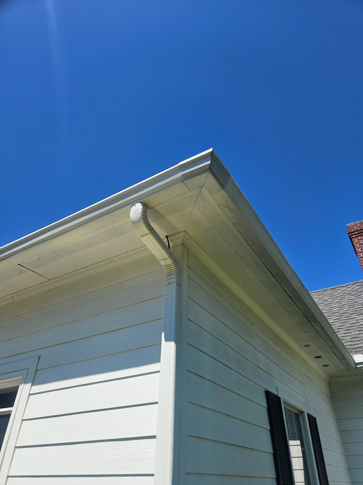 Light blue siding, soffit and gutter against a clear sky